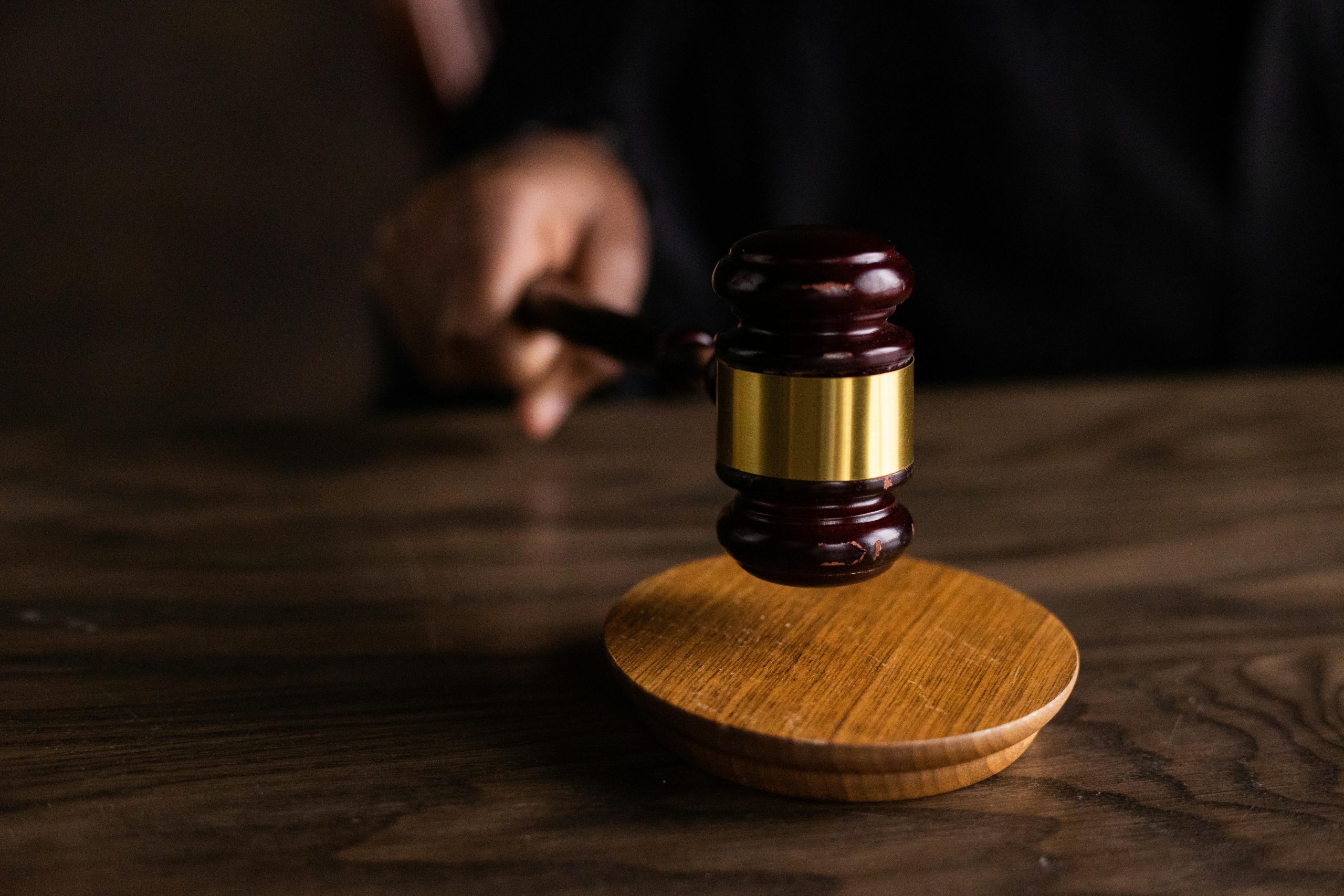 Close up of a judge’s hand holding a wooden gavel above a sound block on a courtroom desk, symbolizing legal judgment and authority.
