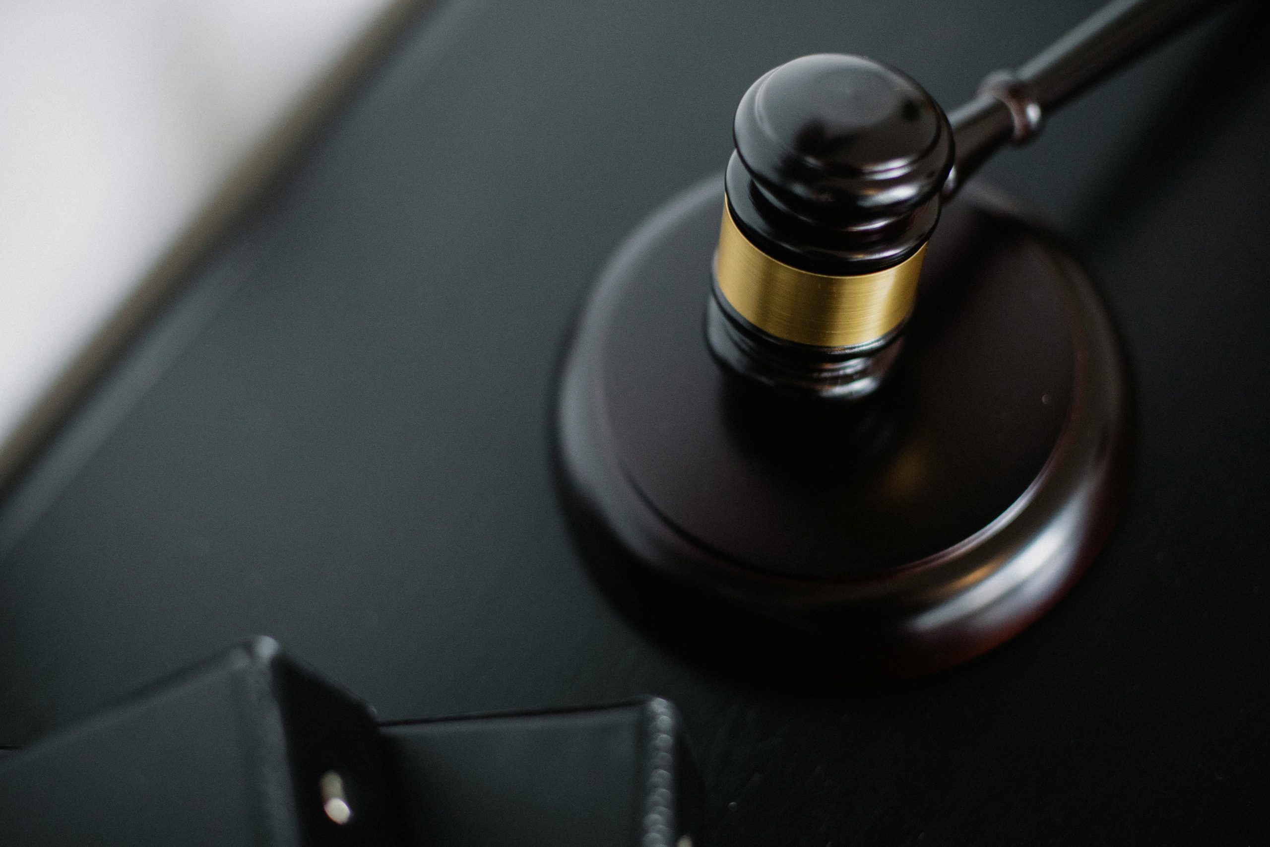 Close-up of a judge’s wooden gavel with a gold band resting on a black sound block, symbolizing justice and courtroom decisions.