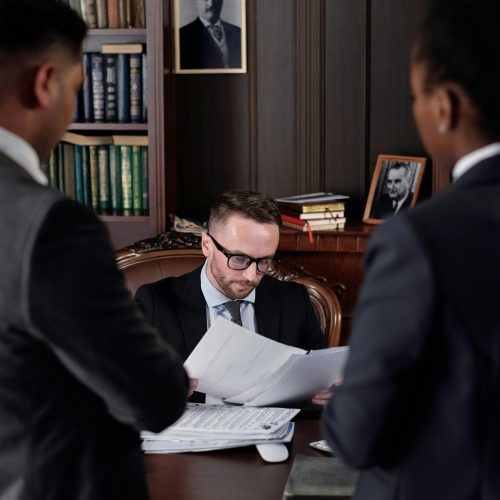 Lawyer reviewing legal paperwork on debt ownership with two clients in a formal office setting