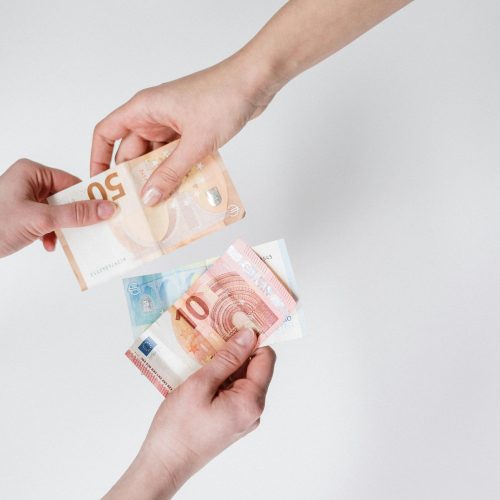 Two hands exchanging euro banknotes, representing debt ownership, repayment, and financial responsibility.