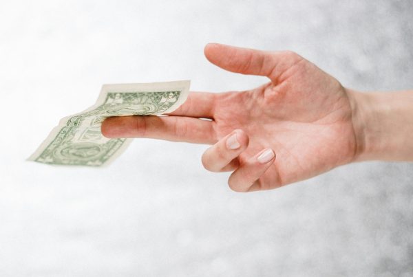 A person holding a dollar bill between two fingers, symbolizing financial stress and the challenge of dealing with creditors.