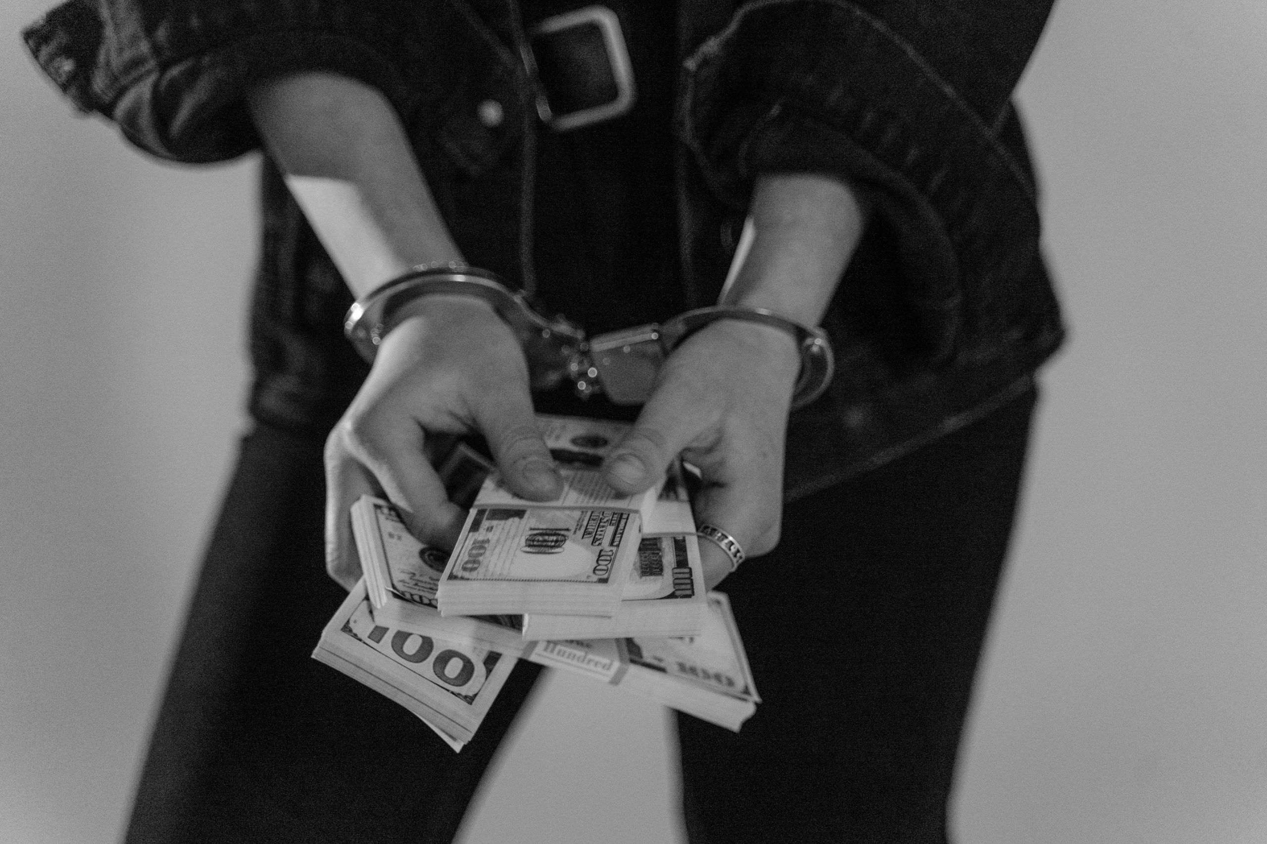 Arrested for debt concept shown with a person in handcuffs holding cash.